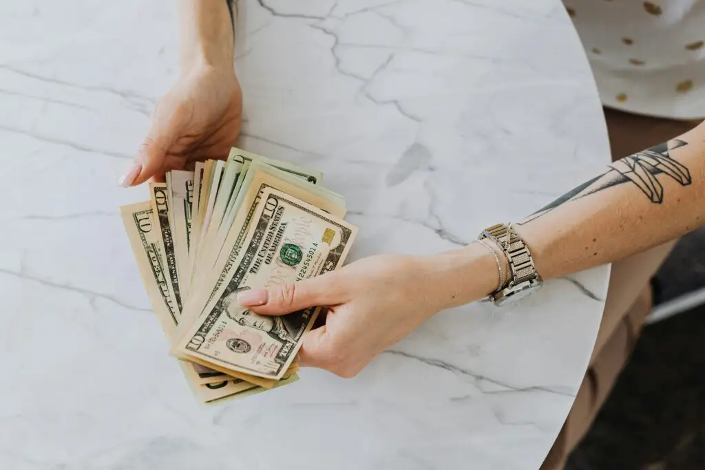 pexels-photo-4968646-4968646 Hands holding and counting US dollar bills on a marble table, depicting wealth and finance.